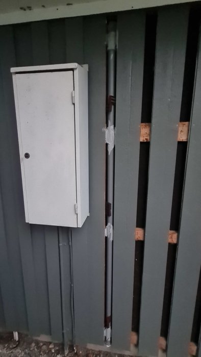 Ø40mm avloppsrör installerat bakom fasadpanel på garage, fixerat med byggfog, bredvid ett stängt skåp.