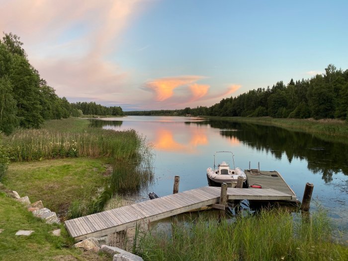 Färgrik solnedgång reflekterad i en lugn sjö med brygga och båt vid kanten.