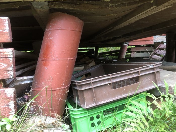 Rörmokningsmaterial under hus: rördelar och plastbackar blandat med träspill.