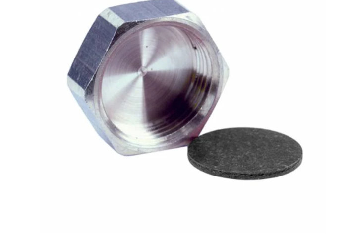 Närbild på en metallisk rördel, möjligtvis en rostfri T-rördel, med en lös packning bredvid.