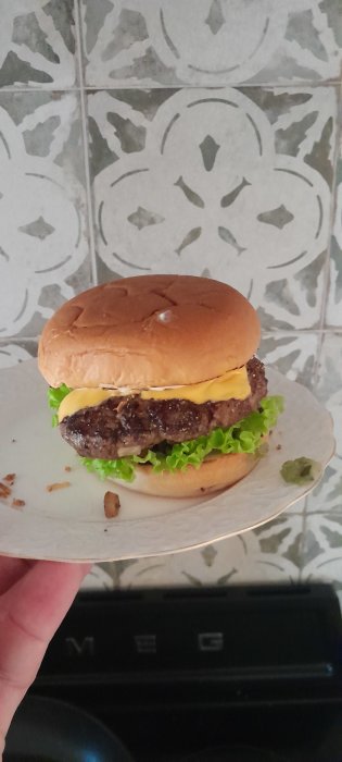 Hemlagad hamburgare med sallad och ost på liten tallrik framför kakelvägg.