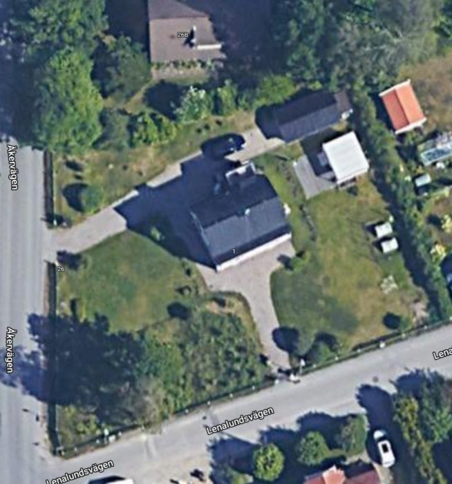 Flygbild över en villa med omgivande trädgård, omgiven av vägar och andra hus.