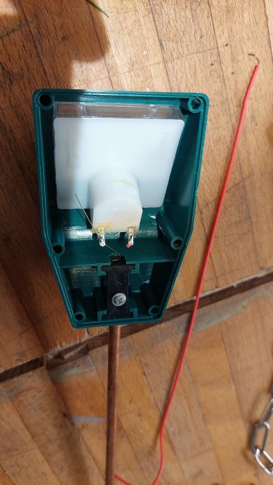 Öppen grön plastlåda med en vit rörelsesensor och avskalade kablar på ett trägolv.