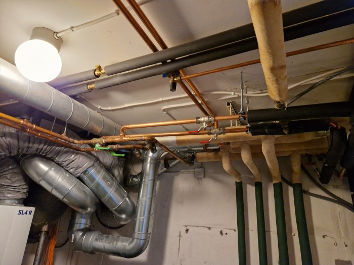 Rördragning i taket med en blandning av koppar- och plastledningar samt isolerade ventilationsslangar.