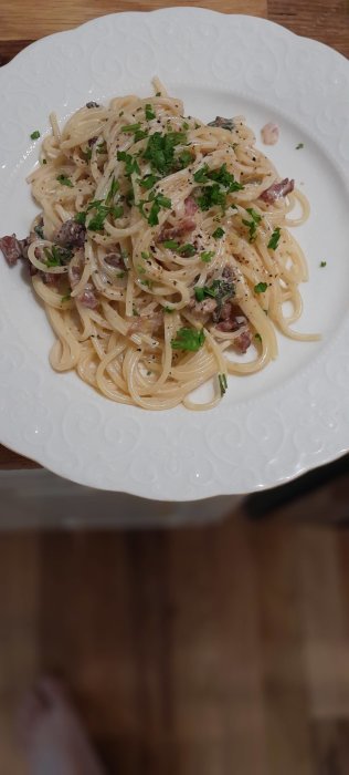 Tallrik med carbonara pasta toppad med hackad persilja, serverad på ett träbord.