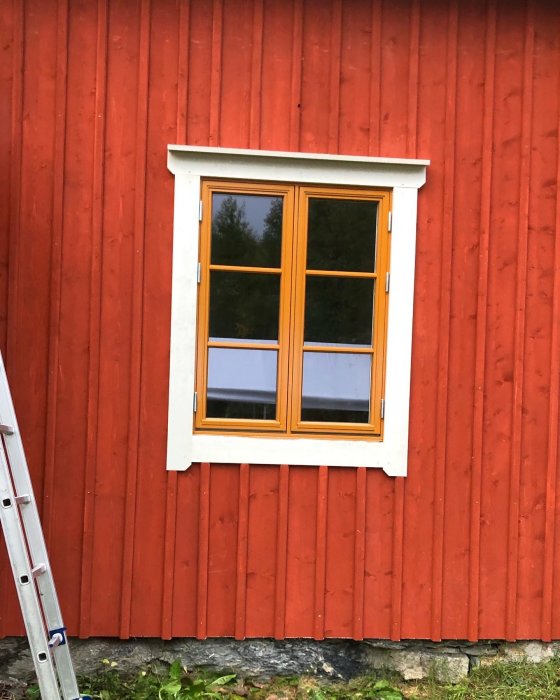 Nymonterade fönsterfoder runt ett stängt fönster på en röd trävägg med stege till vänster.