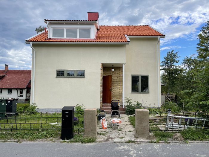 Tvåvåningshus i ljus puts med rött tegeltak, renoveringsmaterial framför huset.