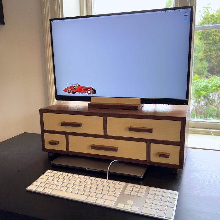 Hemmagjord träskrivbordsorganisatör med lådor framför dator med bildskärm på stativ.