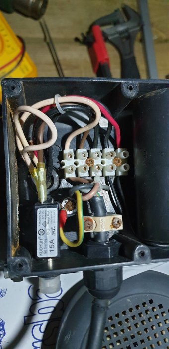 Öppen kopplingsdosa med elektriska ledningar och terminalblock i en vedklyv, inkluderar säkring och jordanslutning.