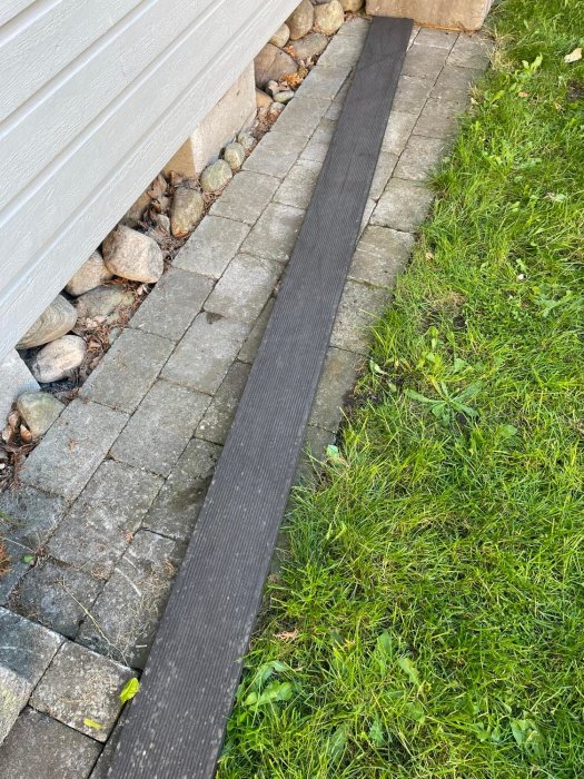 Markduk längs med husvägg för ogräsbekämpning mellan gräsmatta och stenplattor.