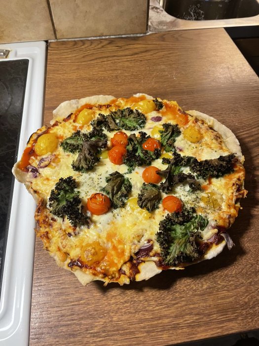 Hemlagad pizza med broccoli, körsbärstomater och ost på ett köksbord.