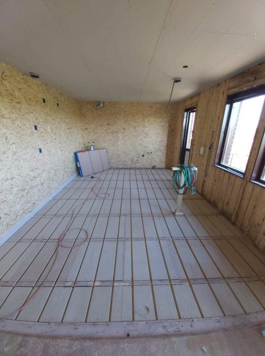 Inredning av ett rum under renovering med isolering på väggar och uppmärkt golv för golvvärmeinstallation.