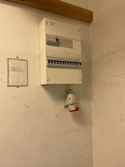 Elcentral med automatsäkringar och jordfelsbrytare monterad på vit vägg med träbjälke ovanför.