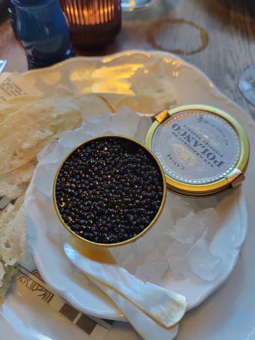 Öppnad burk av kaviar med en sked bredvid på en isbädd, ledsagad av tunna kexskivor.