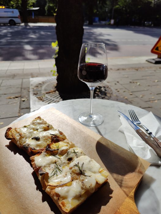 Ostdränkt bröd och glas rödvin på uteservering i Stockholm, soligt dagtid.