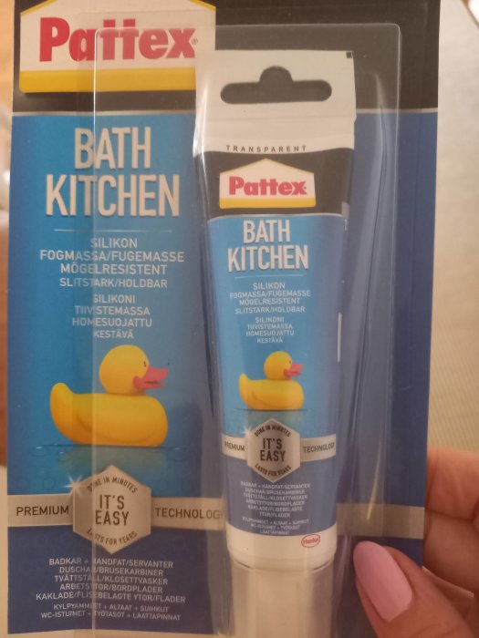 Ett paket med Pattex Bath Kitchen silikonfogmassa hålls i handen, transparent och mögelresistent.