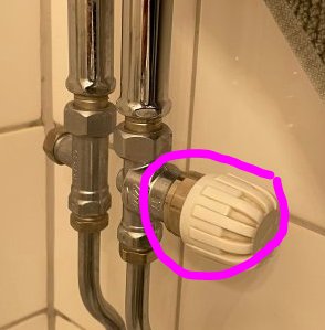 Närinställd bild av en handdukstork ansluten till rör med synlig termostatventil markerad med en rosa cirkel.