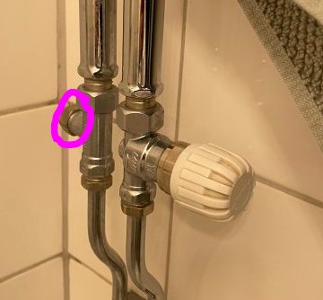 Närbild av en handdukstork ansluten med ventiler och rör i ett badrum markerad med en cirkel runt en ventil.
