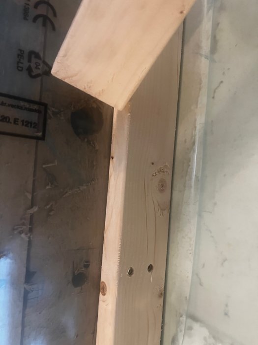 Byggplatsdetalj med träreglar fastskruvade på en vägg med synlig plastisolering och skyddsplast på butylband.