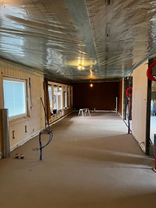 Byggplats inuti ett hus med installerad plastfolie i taket och synliga väggvinklar, elinstallationer pågår.