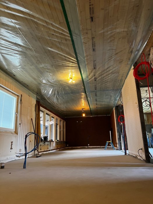 Renoveringsarbete med plastfolie fäst vid tak med överlappande skarv och uppsatta elinstallationer längs väggar.