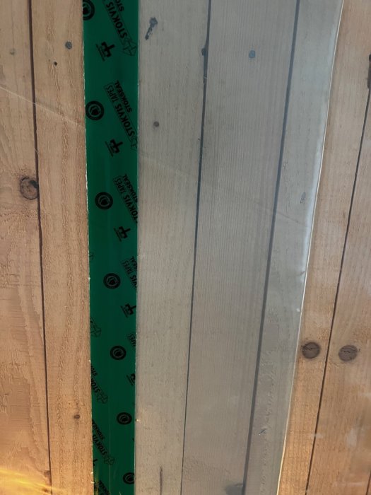 En grön byggtape längs en träväggvinkel med skyddsplast delvis borttagen, redo för tätning.