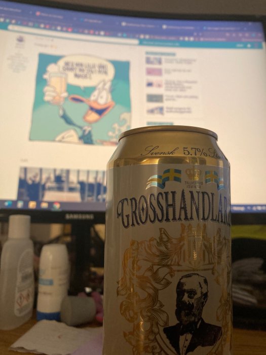 Burk öl i förgrunden med skärmen i bakgrunden som visar en animerad figur som höjer en skål.