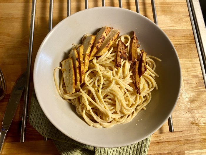 Skål med spaghetti och gräddsås toppad med stekta oumph-strips på träbord.