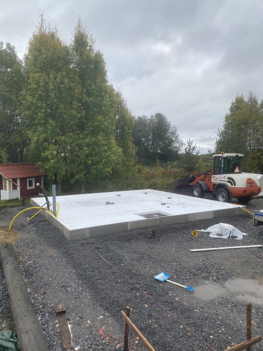 Byggplats med nästan komplett första lager av isolering och förberedd betonggjutning, traktor i bakgrunden.