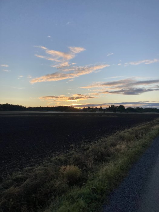 Soluppgång över ett plöjt fält med en klarblå himmel och spridda moln.