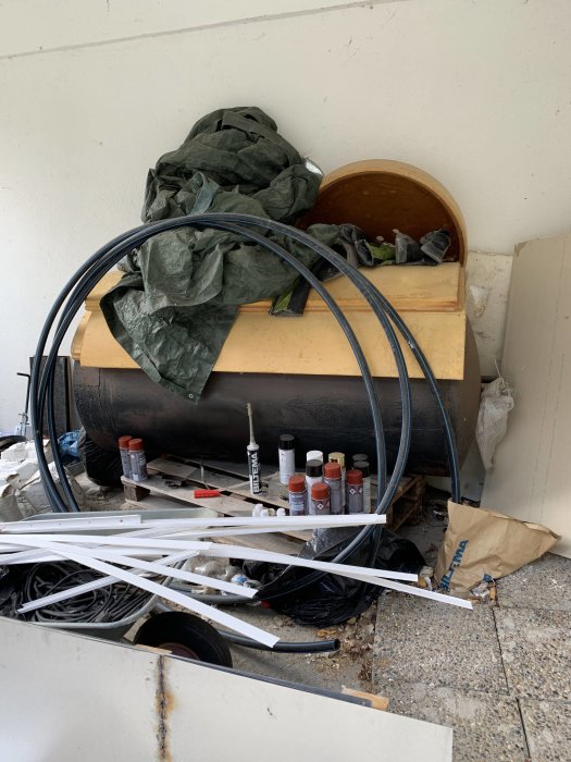 Oorganiserad samling av byggmaterial med kablar, sprayburkar och träbitar.