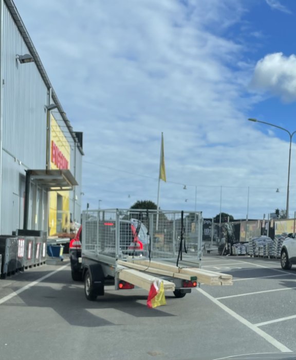 Last på släpvagn säkrad med spännband och gummistropp utanför en Byggmax-butik.