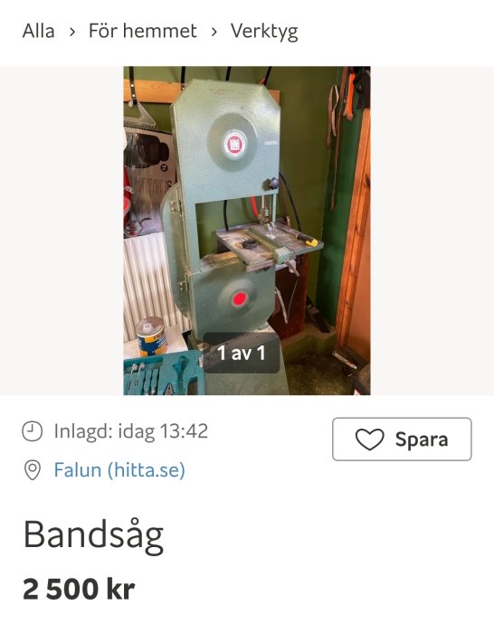 Vertikal bandsåg i verkstaden med grönt hölje och arbetsbord.