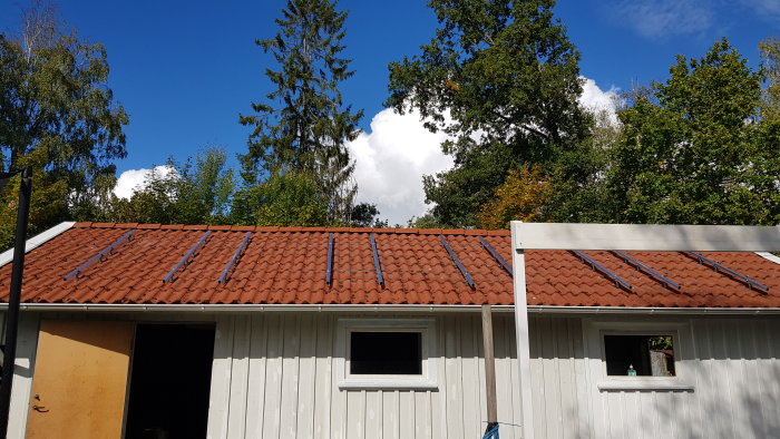 Garage med tegeltak och nyligen monterade fästen för solpaneler under en klar himmel.