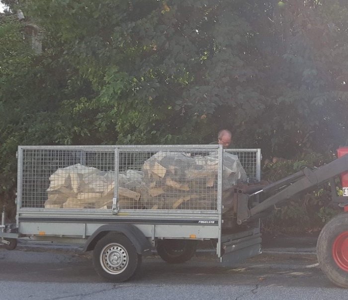 En släpvagn lastad med torr ved och en person som använder en gaffeltruck för att lasta av veden.