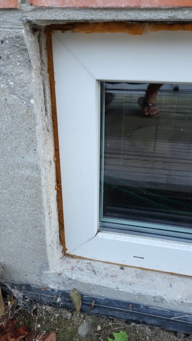 Fönsterinstallation med oskummat mellanrum mellan ram och vägg, synligt murbruk och löv på fönsterblecket.