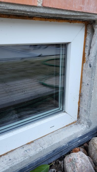 Närbild på ett fönsters nedre karm med synlig isolering och murbruk.