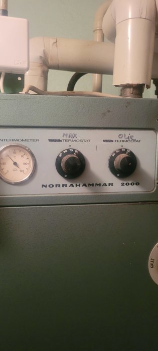 Värmepannans kontrollpanel med termometer och termostater märkta 'NORRAHAMMAR 2000'.