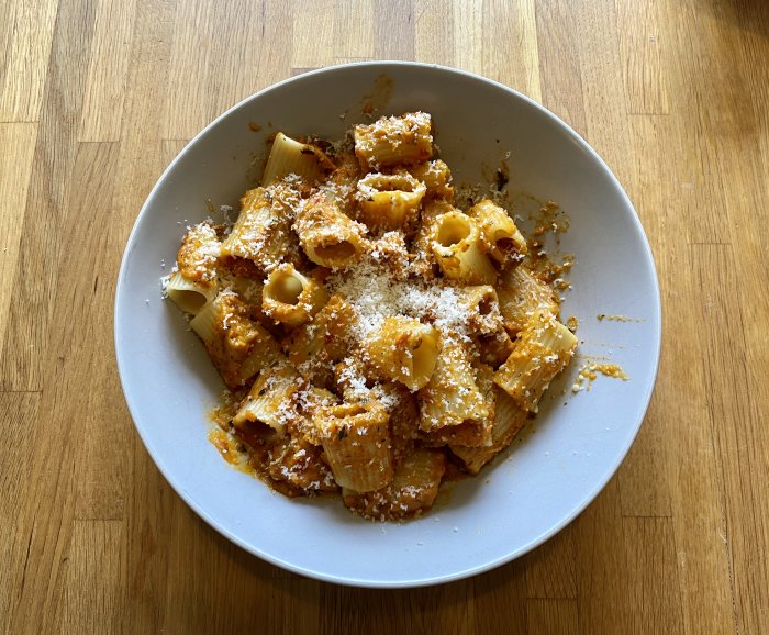 En tallrik pasta med vegetabilisk sås och strödd parmesan på ett träbord.