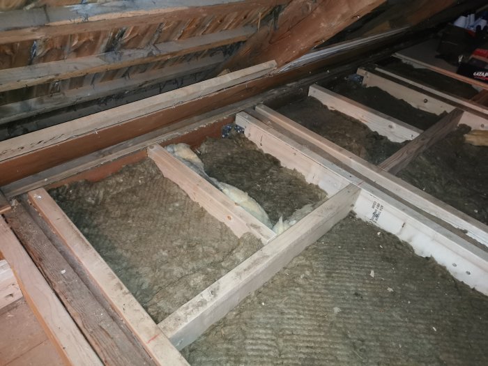 Renoverat golv med ny golvkonstruktion och isoleringsmaterial i ett orenoverat vindsrum.
