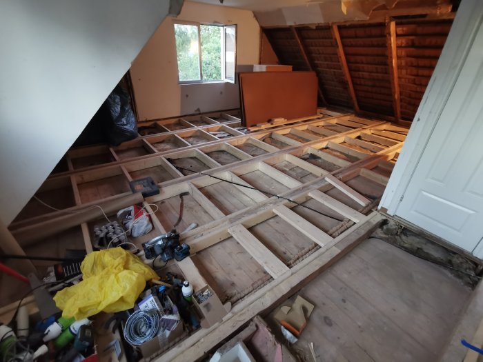 Öppet golv i ett renoveringsprojekt med träbjälkar, verktyg och byggmaterial, och delvis lagda golvspånskivor.