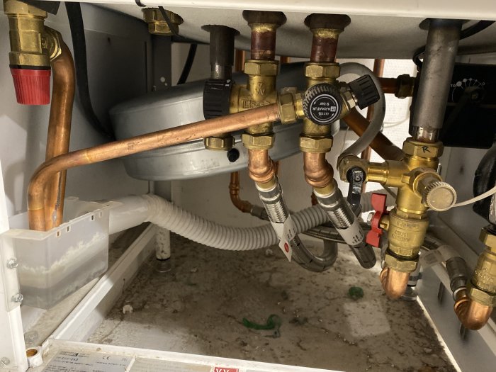 Under-sink plumbing with copper pipes, valves, and pressure gauge needing adjustment.