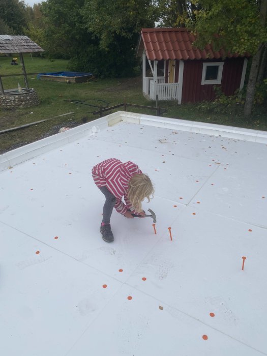 Barn hjälper till att spika cellplastspik i byggprojekt för golvvärmeinstallation utomhus.