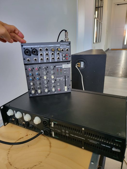 En hand pekar på en liten Phonic mixer ovanpå en Lab.gruppen förstärkare på bord.