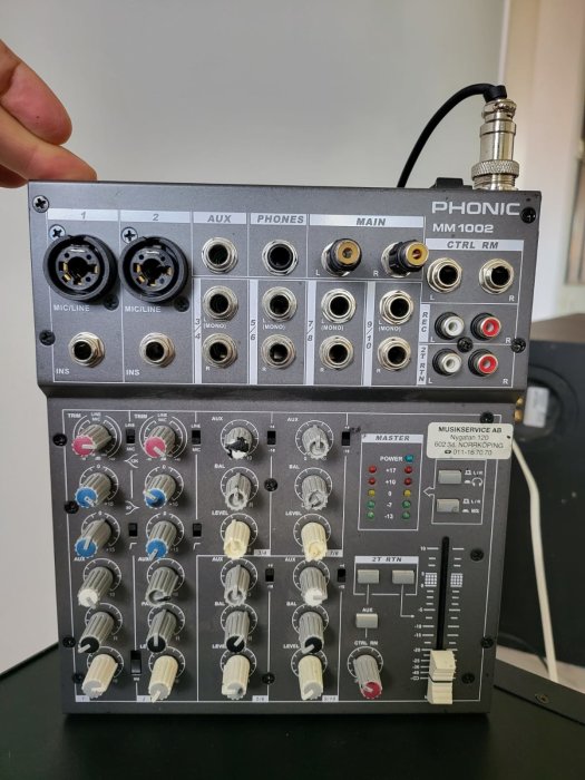 Phonic ljudmixer med flera reglage och input-uttag, inklusive XLR och RCA, i fokus med en person som håller i enheten.