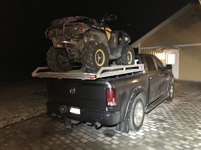 En ATV lastad ovanpå ett kort flak på en svart Dodge RAM-pickup under nattbelysning.
