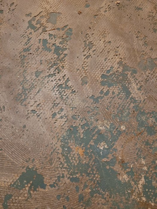 Närbild av ett slitet betonggolv med delvis avskalad grön färg och synliga slitagespår.