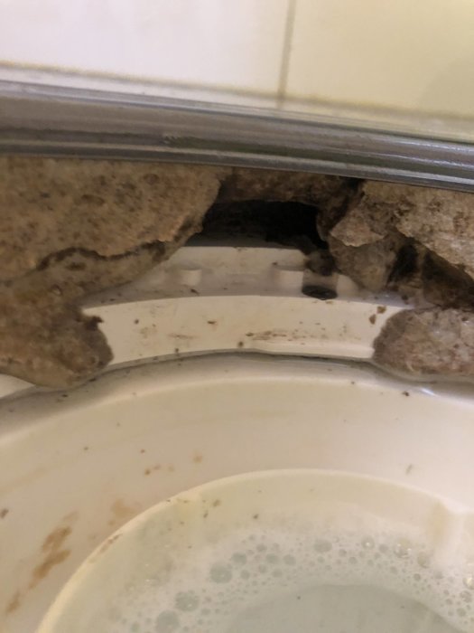 Hål i vägg vid kakellist ovanför badrumshandfat med synlig rörisolering och spår av smuts.