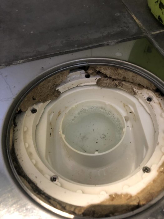 Närbild på ett smutsigt diskhoavlopp med synliga rester och kalkavlagringar.