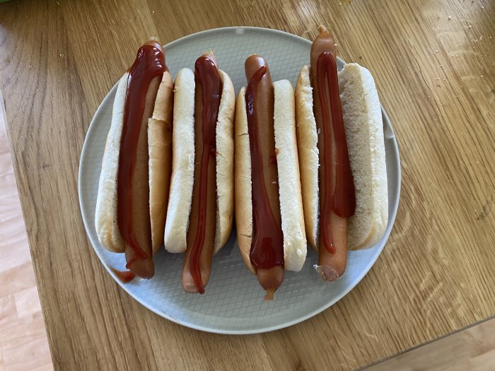 En tallrik med fem korvar i bröd med ketchup på en träyta.